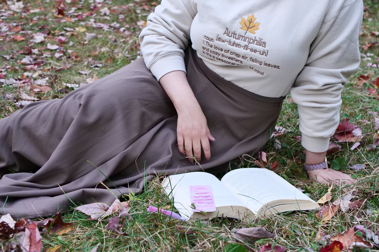 Person sitting on grass with an open book, wearing a sweatshirt with text.