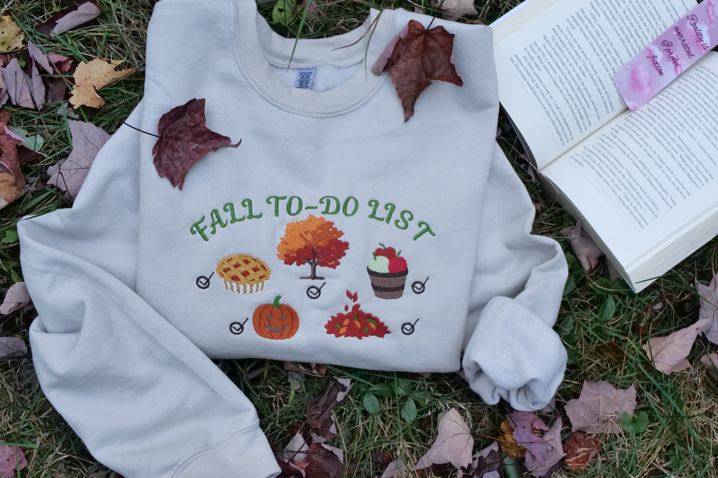 White sweatshirt with 'Fall To-Do List' design on grass with leaves