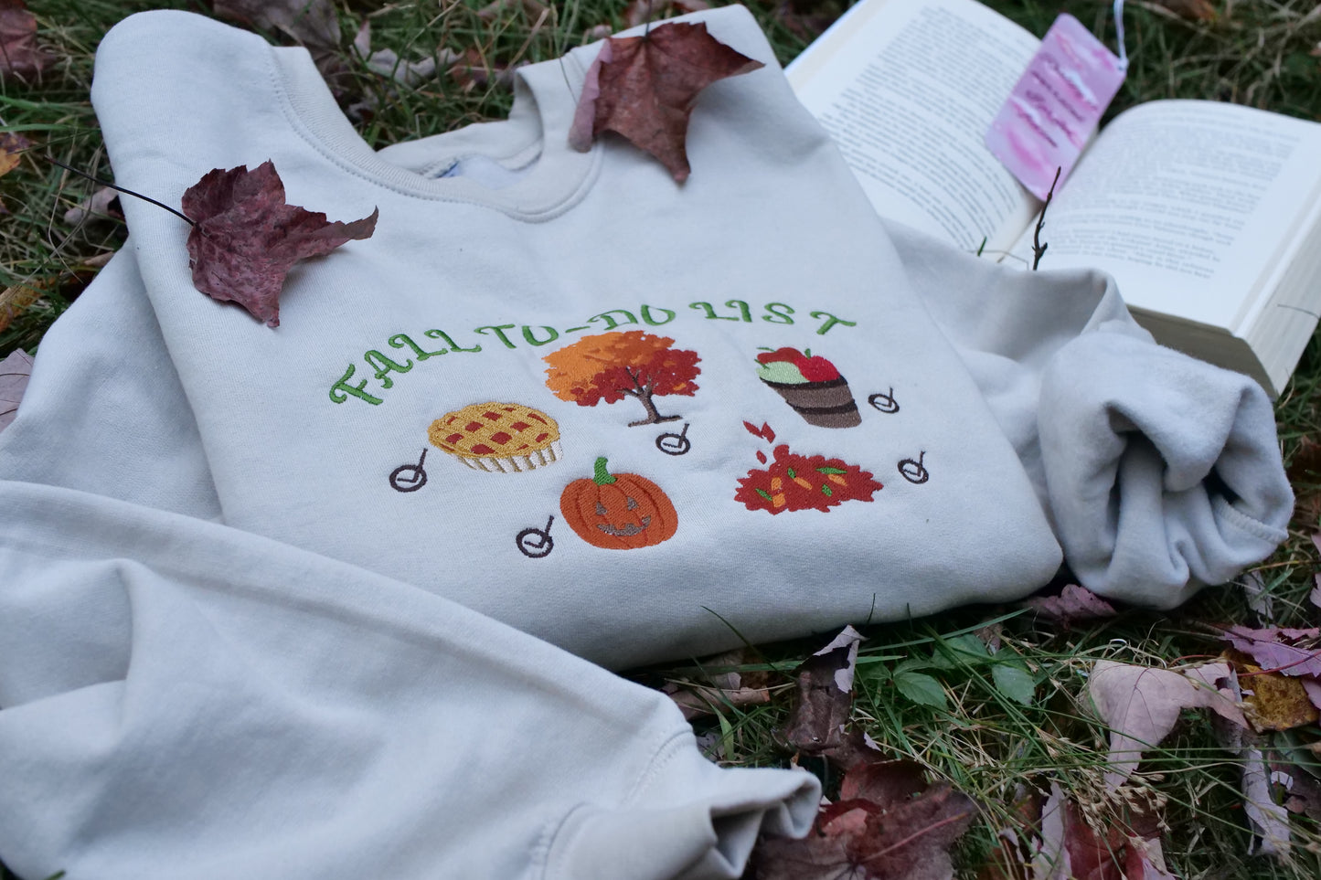 sand sweatshirt with autumn-themed embroidery on grass with leaves