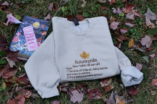 sand color sweatshirt with 'Autumnphilia' text and definition on grass with leaves