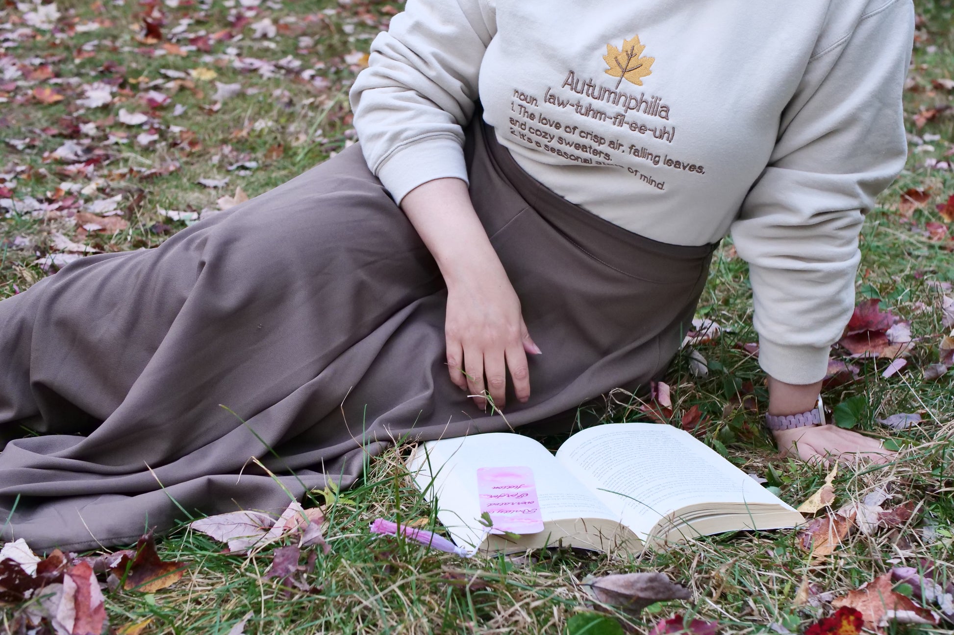 Person sitting on grass with an open book, wearing a sweatshirt with text.