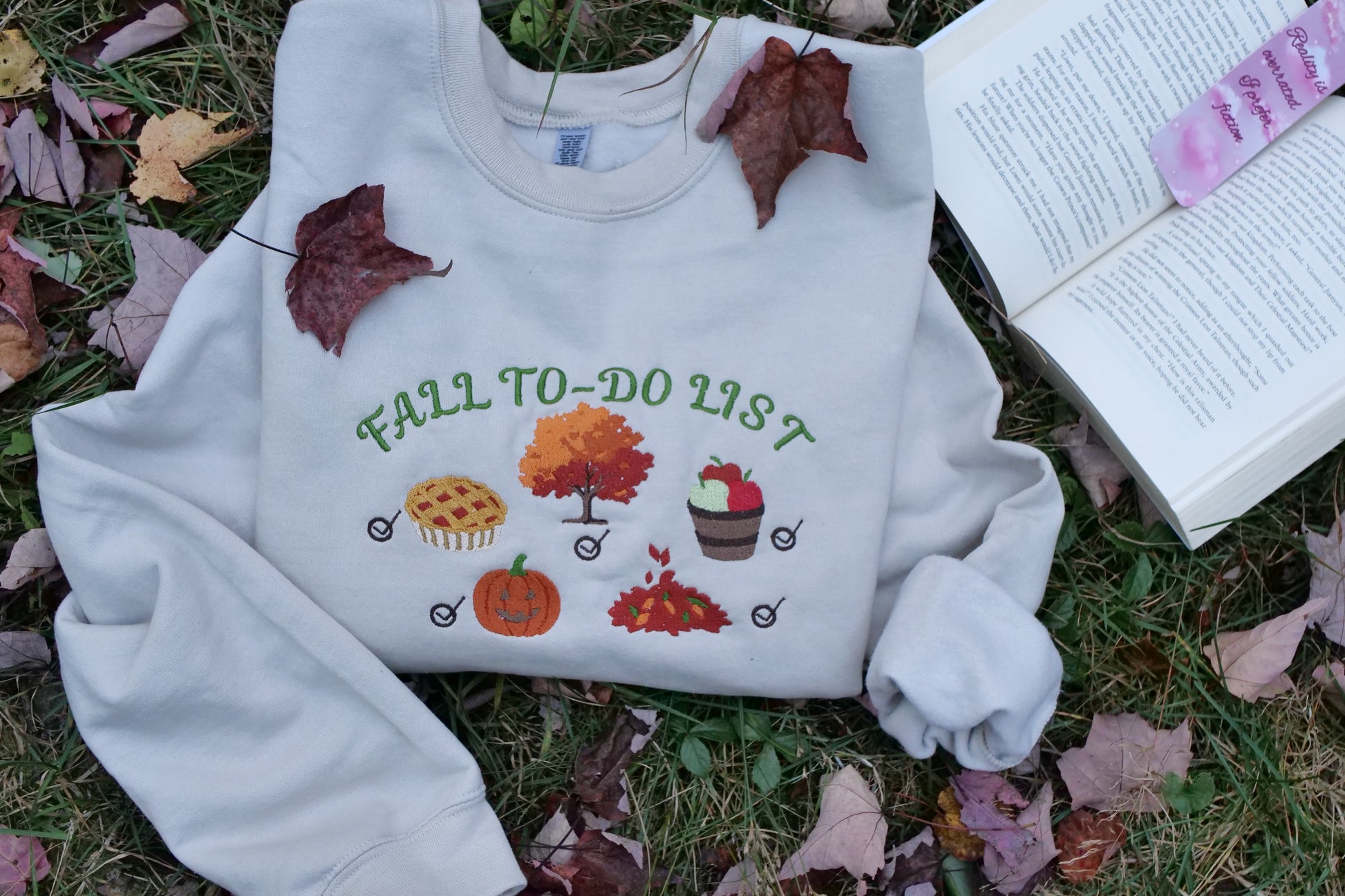 White sweatshirt with 'Fall To-Do List' design on grass with leaves